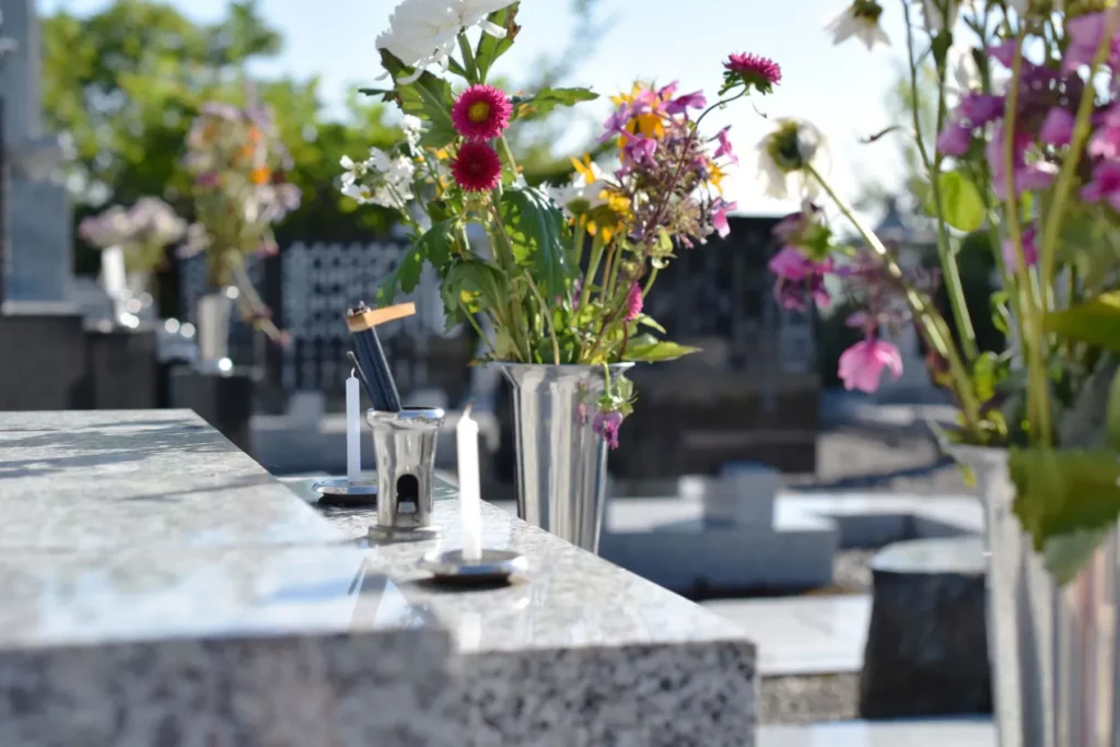 Bougies et vase de fleurs champêtres posés sur une pierre tombale en granite dans un cimetière.
