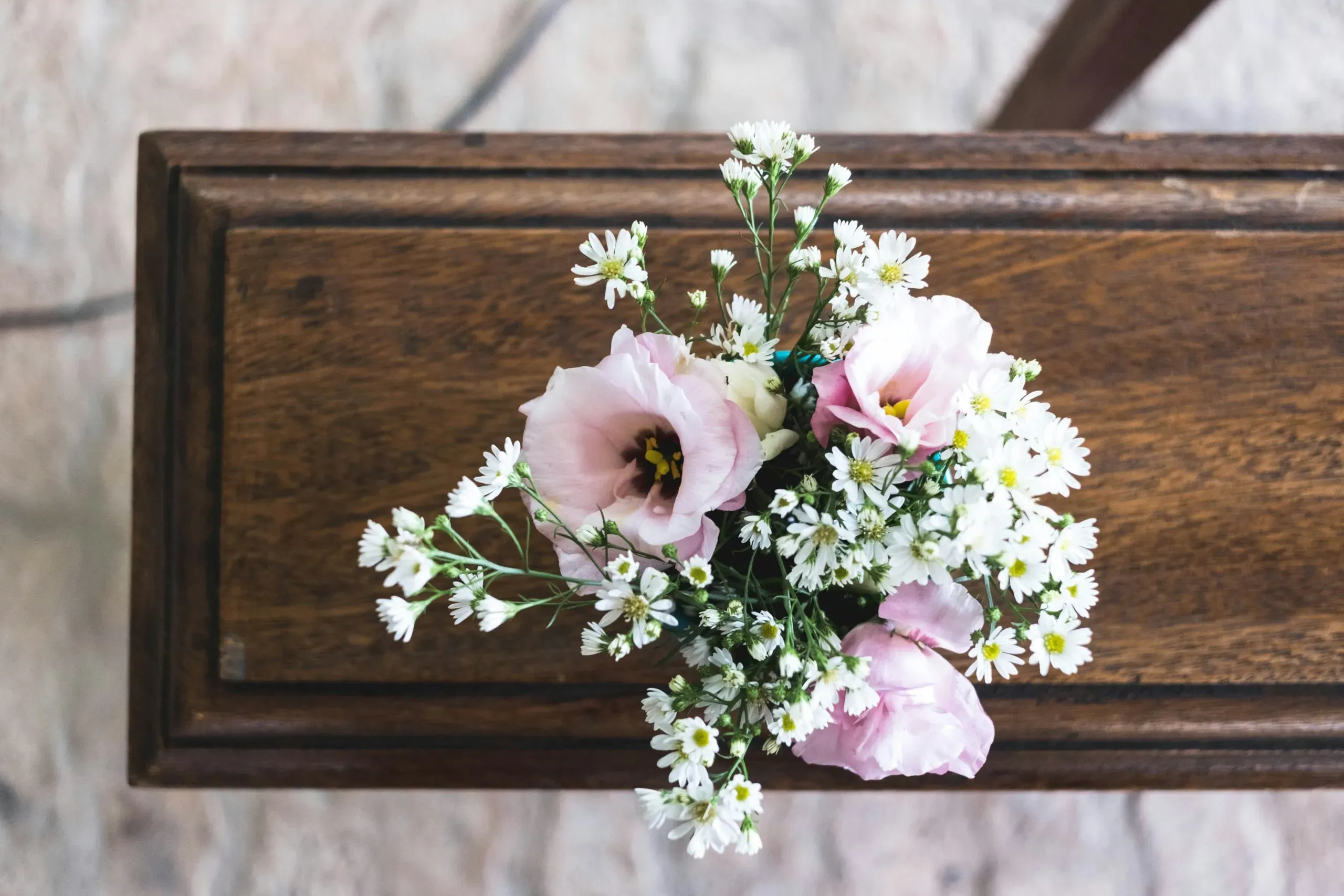 Bouquet de petites fleurs blanches et roses posé sur un cercueil en bois foncé.