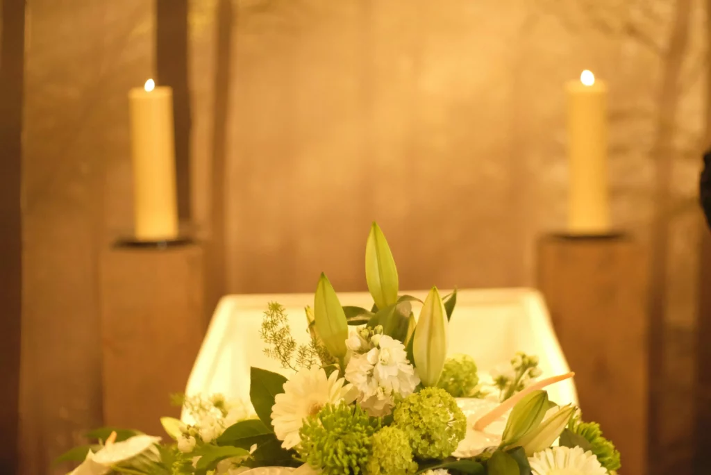 Composition florale blanche et verte disposée devant des bougies d'un lieu de culte.