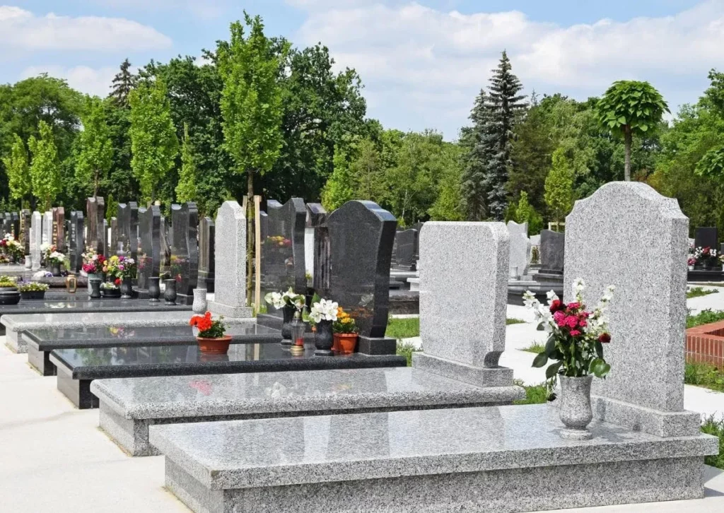 Alignement de monuments et pierres tombales en granite gris et noir fleuris dans un cimetière paysager.