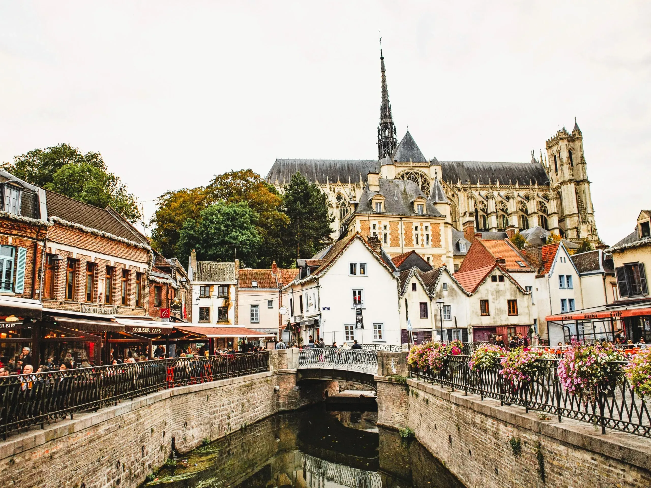 Vue du quartier historique d'Amiens avec canal et cathédrale en arrière-plan.